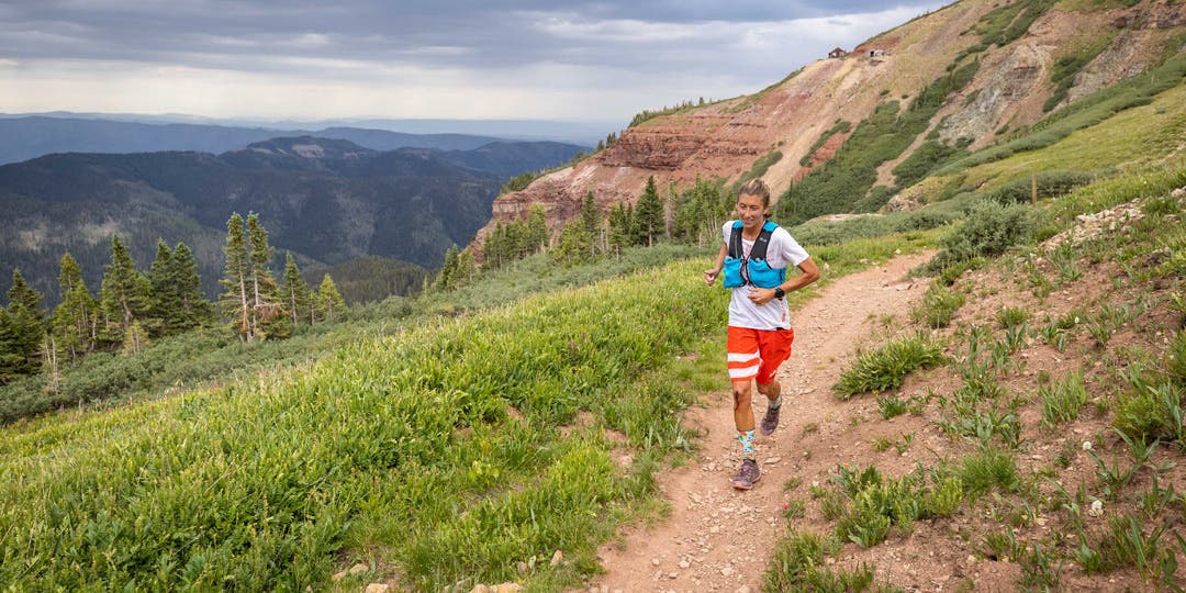 Courtney Dauwalter running down a single track trail in the mountains at high elevation.