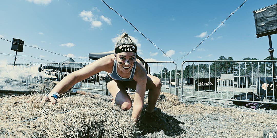 Alexandra Mueller puasing to kneel down on some hay during an obstacle course race.