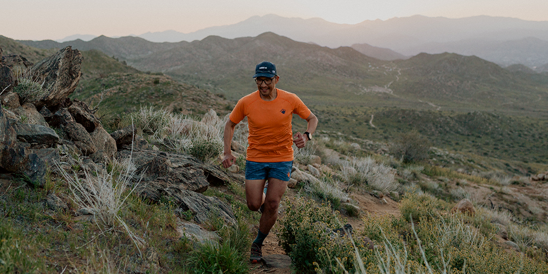 Korean American Athlete Phil Shin running on a high desert trail with mountains in the background.