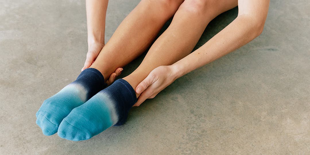 A person sitting on the ground pointing their feet while wearing Injinji Grip Full Foot No-Show.