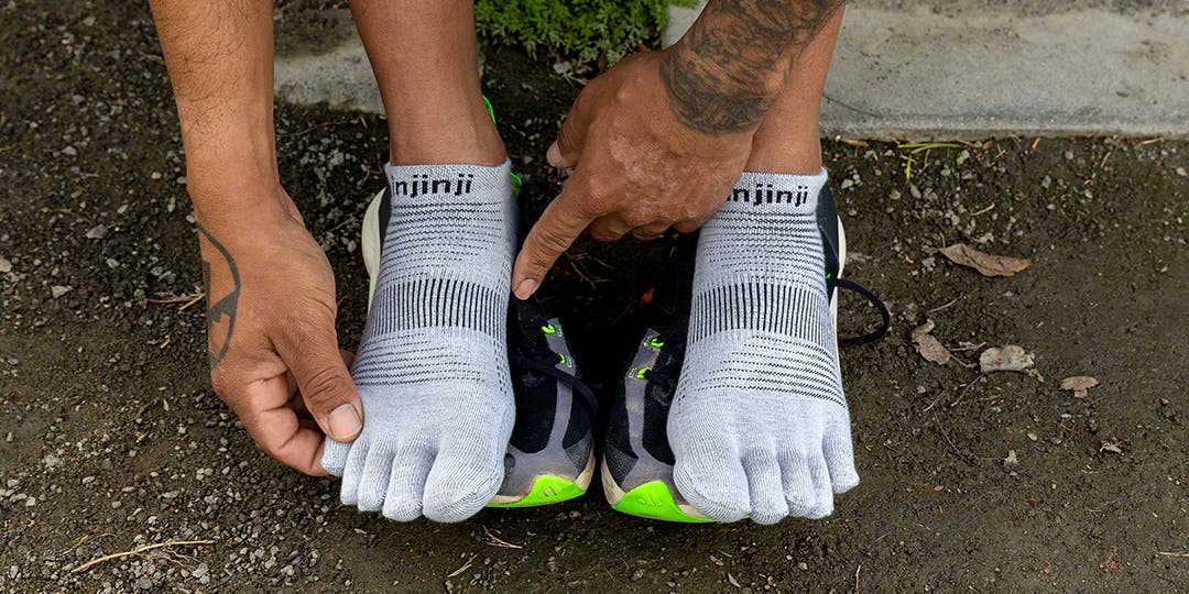 A person bent over their feet adjusting their Injinji Run Lightweight No-Show toesocks with their running shoes resting beneath their feet.