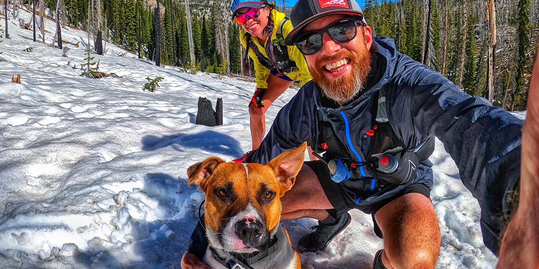 Trish and Garrick Arends with their dog Olly on a snow trail in the woods on a bluebird day.