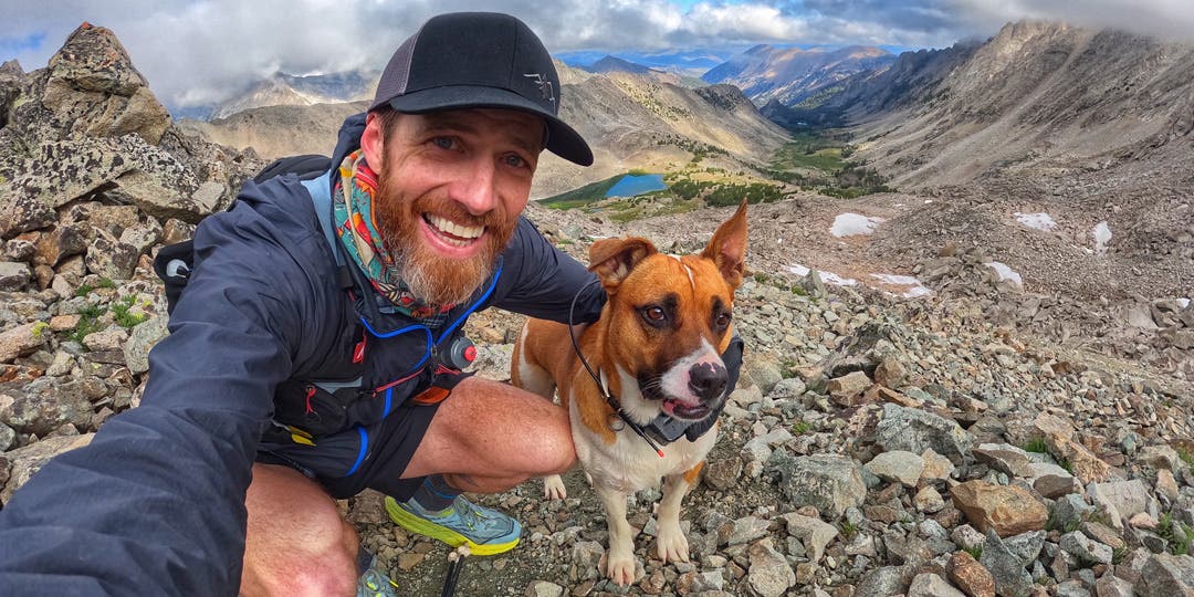 Garrick Arends taking a selfie with his dog Olly at the top of a trail above an alpine lake.