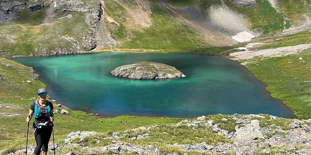 Team Injinji athlete Angela Shartel posing in front of an alpine lake at Hardrock 100 ultramarathon.