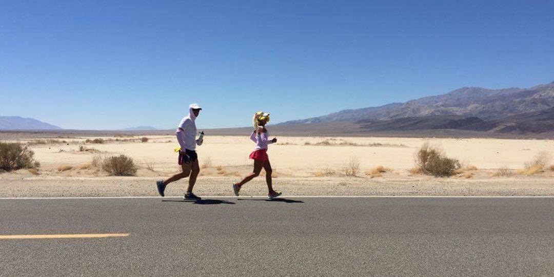 Man and woman running on the asphalted road surrounded by a desert landscape