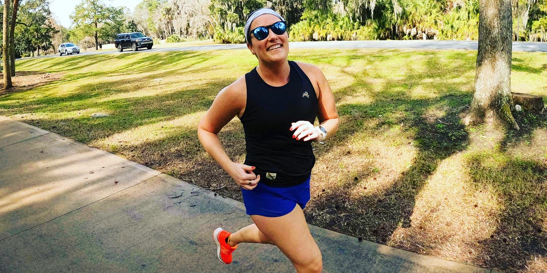 Female marathoner training on a sunny day surrounding by green grass and trees. 