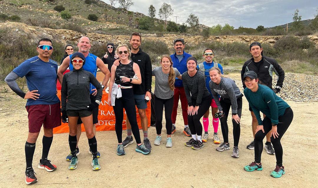 A group of San Diego Track Club runners posing after a group run on a sandy trail.