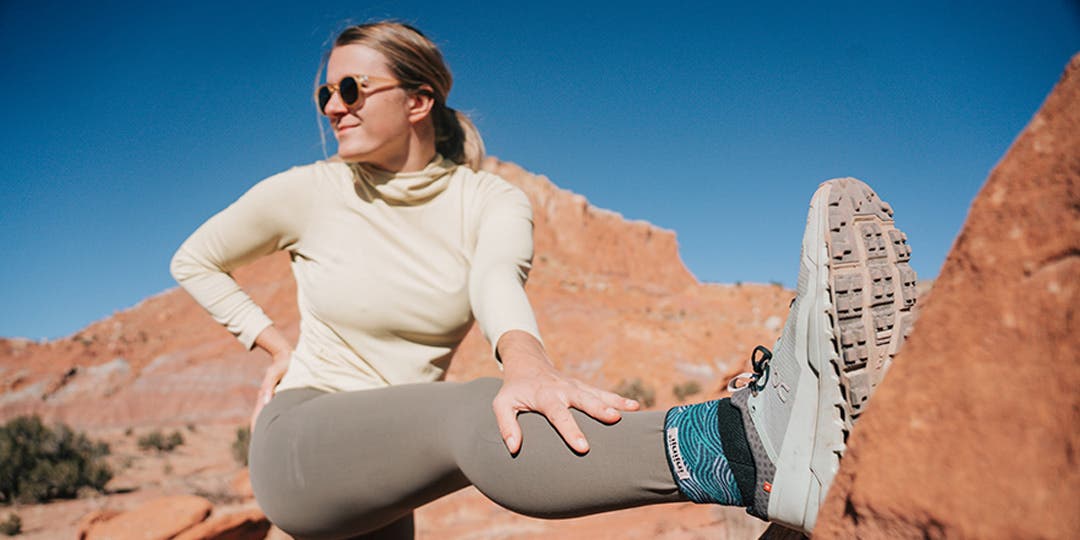 Artist Kika MacFarlane stretching her legs against a large red rock in Moab, Utah.