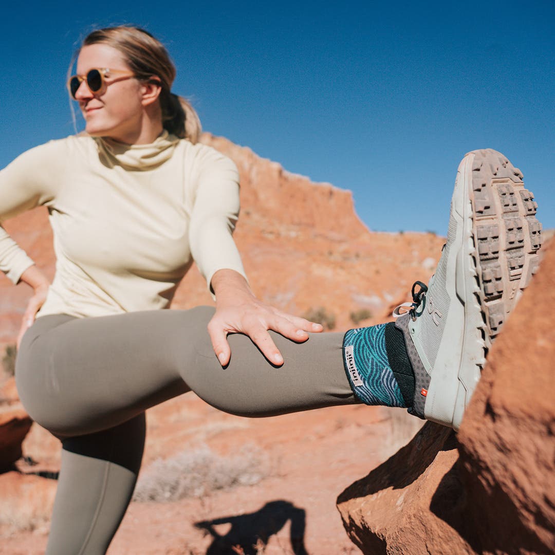 Artist Kika MacFarlane stretching her legs against a large red rock in Moab, Utah.