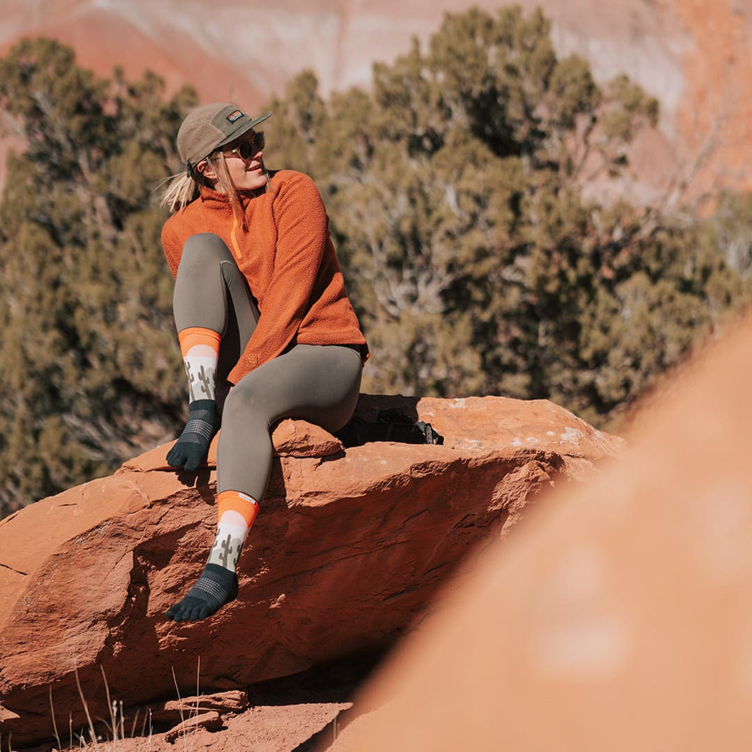 Kika MacFarlane artist behind Injinji first Artist Designed series, The Canyons collection, sitting on a large red rock in Moab, Utah.