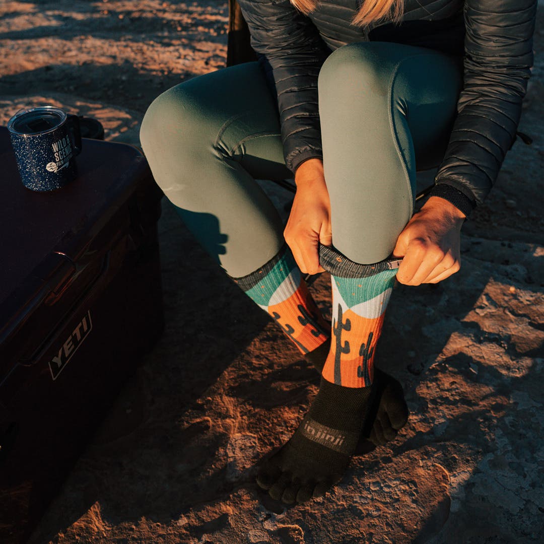 Artist Kika MacFarlane sitting down and pulling the Artist Designed Men's Crew sock in Midnight up her calf.