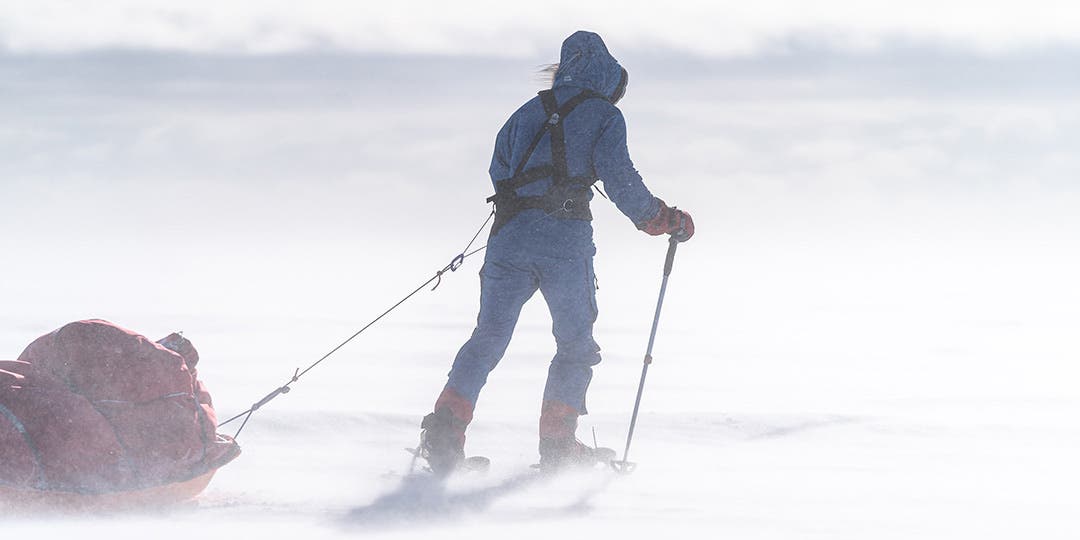 Team Injinji Athlete Meghan Buchanan dressed in full ice mountaineering gear hiking her way over a mountain during a wind storm.