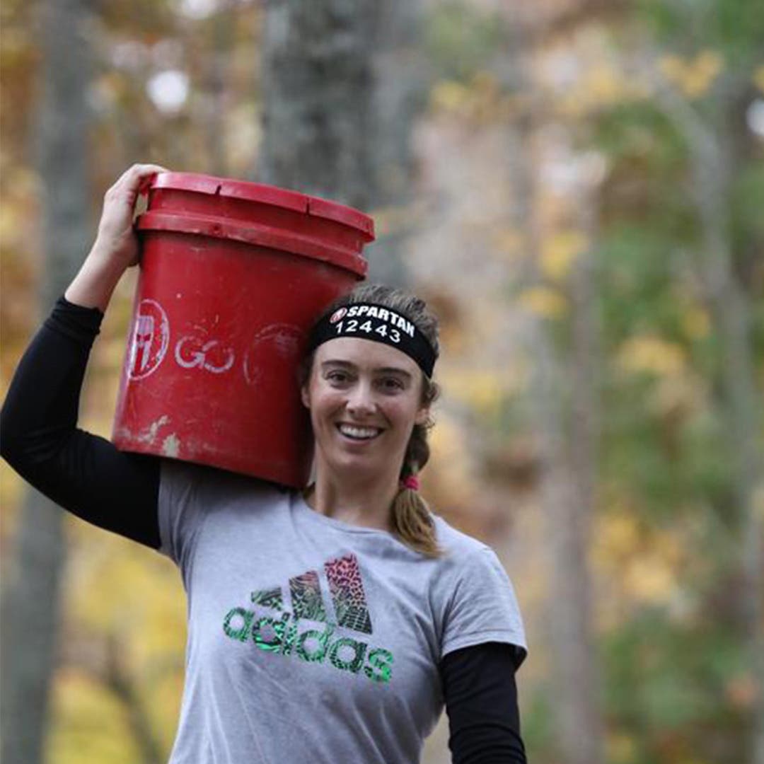 Alexandra Mueller carrying a weighted bucket over her shoulder during an obstacle course race.