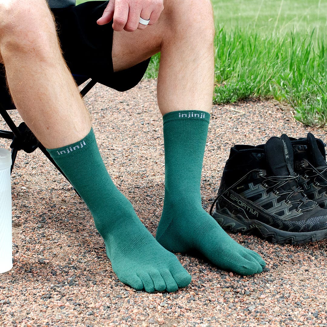 A hiker sitting in a camp chair wearing Injinji Liner Crew socks in Agave.