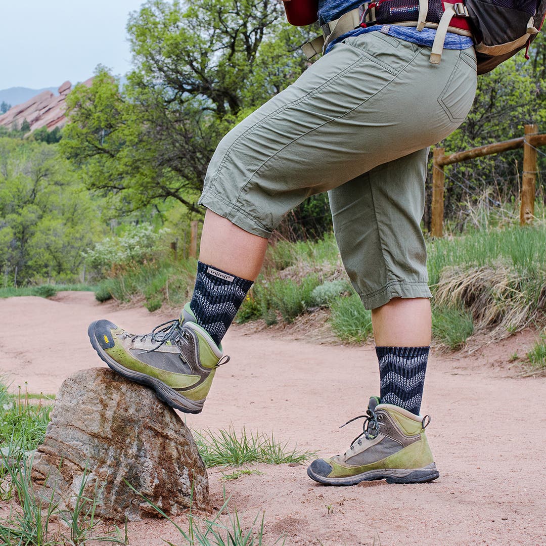 A hiker resting their foot on a rock wearing Injinji Outdoor Midweight Crew Wool socks underneath their hiking boots.