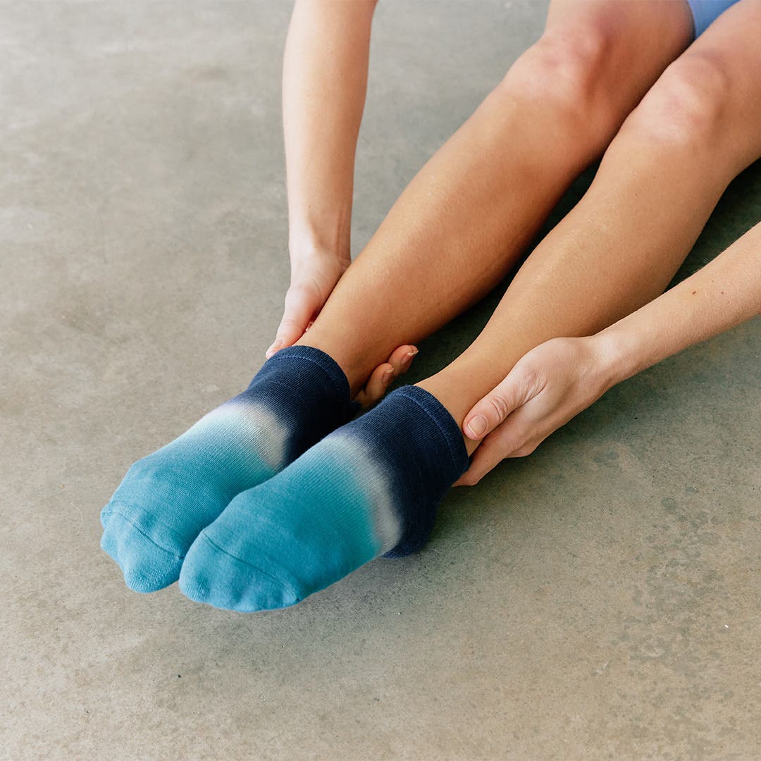 A person sitting on the ground pointing their feet while wearing Injinji Grip Full Foot No-Show.