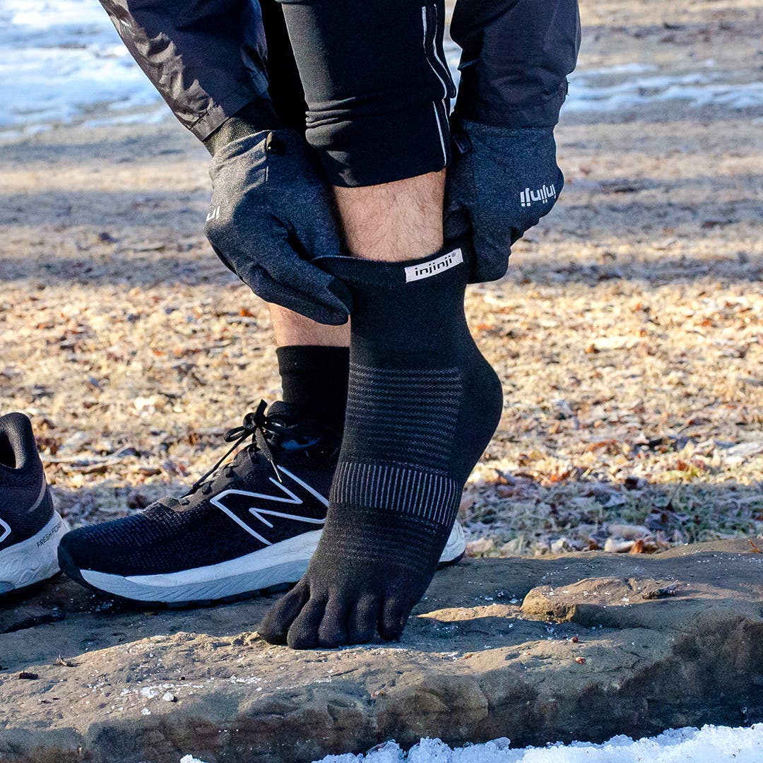 Close up view of someone's feet as they adjust their Injinji Run Lightweight Mini-Crew toesocks. 