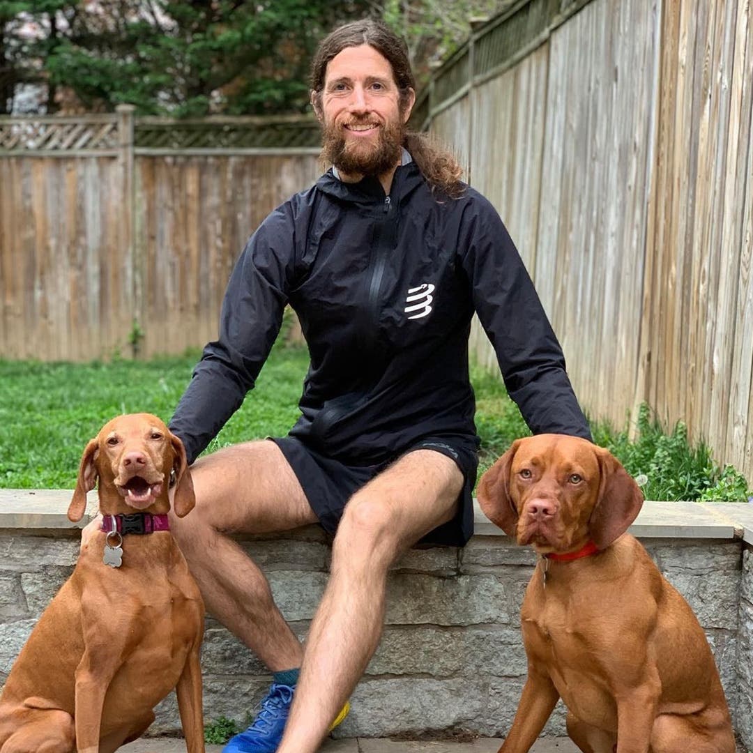 Mike Wardian sitting on a concrete bench with his two vizla dogs Rosie and Bash.
