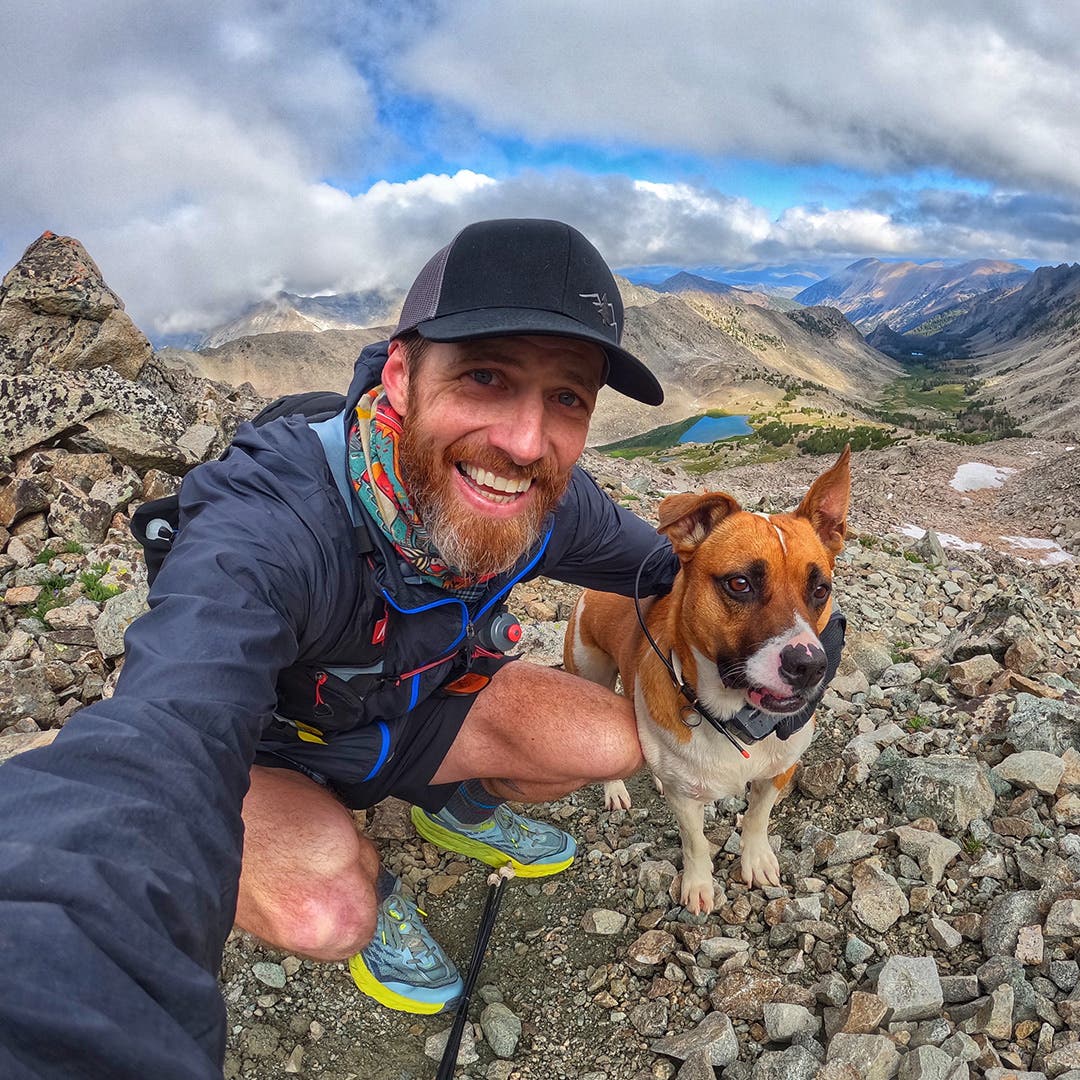 Garrick Arends taking a selfie with his dog Olly at the top of a trail above an alpine lake.