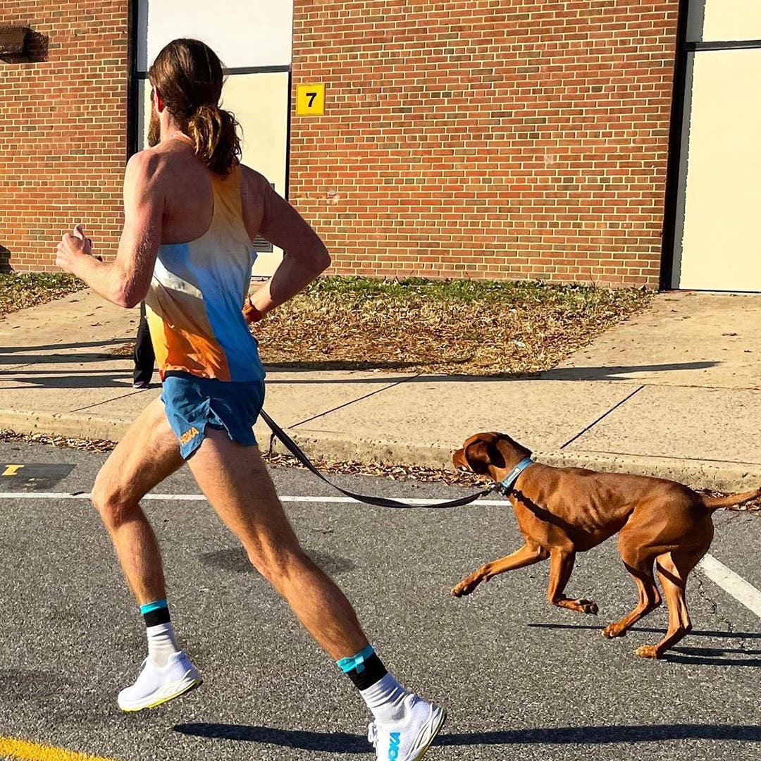 Mike Wardian running on pavement with his dog while holding his leash.