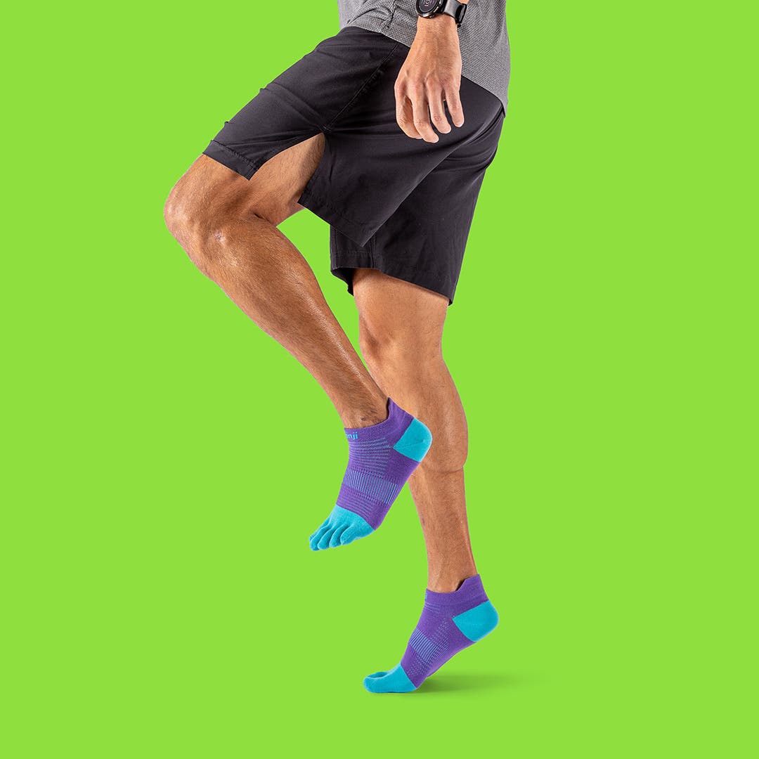 A man performing knee-highs wearing black shorts and the Injinji Run Lightweight No-Show toesocks in the color Lupine. 