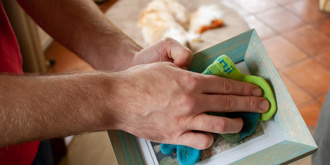 A man cleaning a picture frame using an old Injinji toesock.