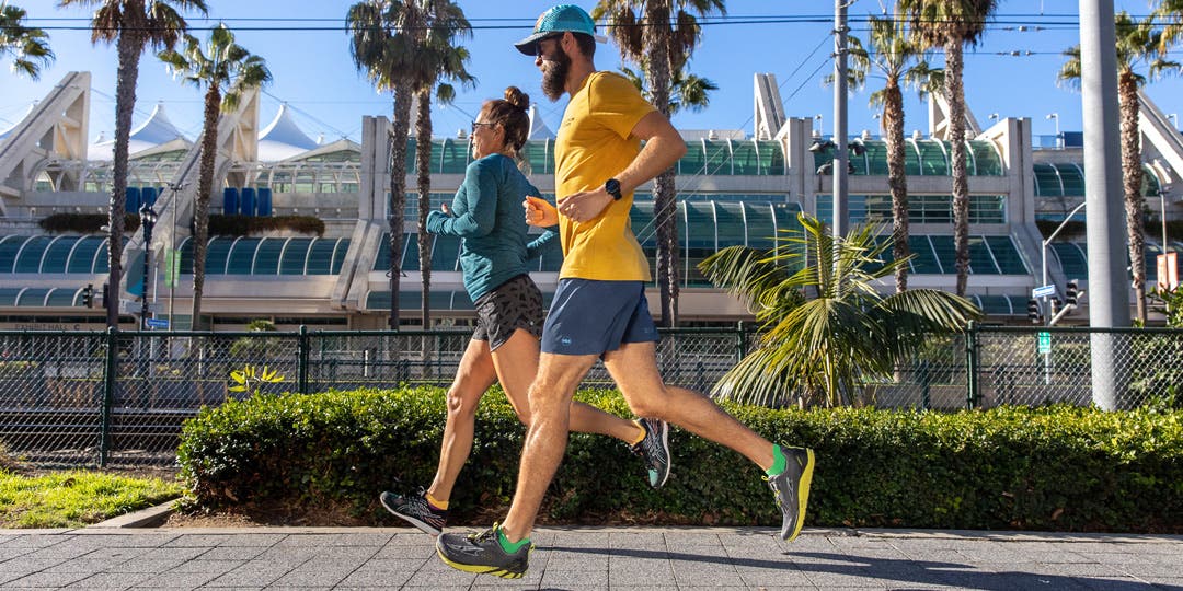 A man and woman running on pavement in San Diego with palm trees and blue skies in the background, sporting Injinji Run Lightweight No-Show toesocks. 