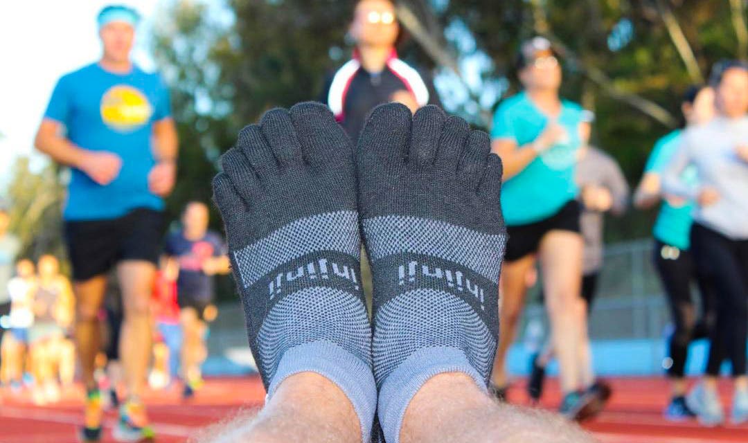 Closeup of someone's feet wearing the Injinji Trail Midweight Mini-Crew in Granite, with track runners running in the background.