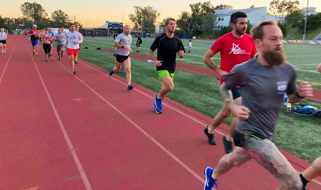 Members of the San Diego Track Club running on a track at dusk.