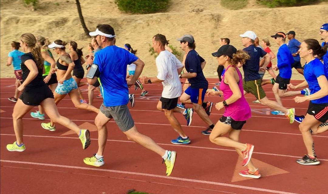 A group of 15 people in full stride running on a track.