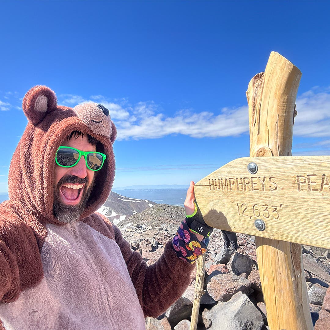 Peter Mortimer wearing a fuzzy bear onesie taking selfie with the Humphrey's Peak trail sign at 12,633 ft.