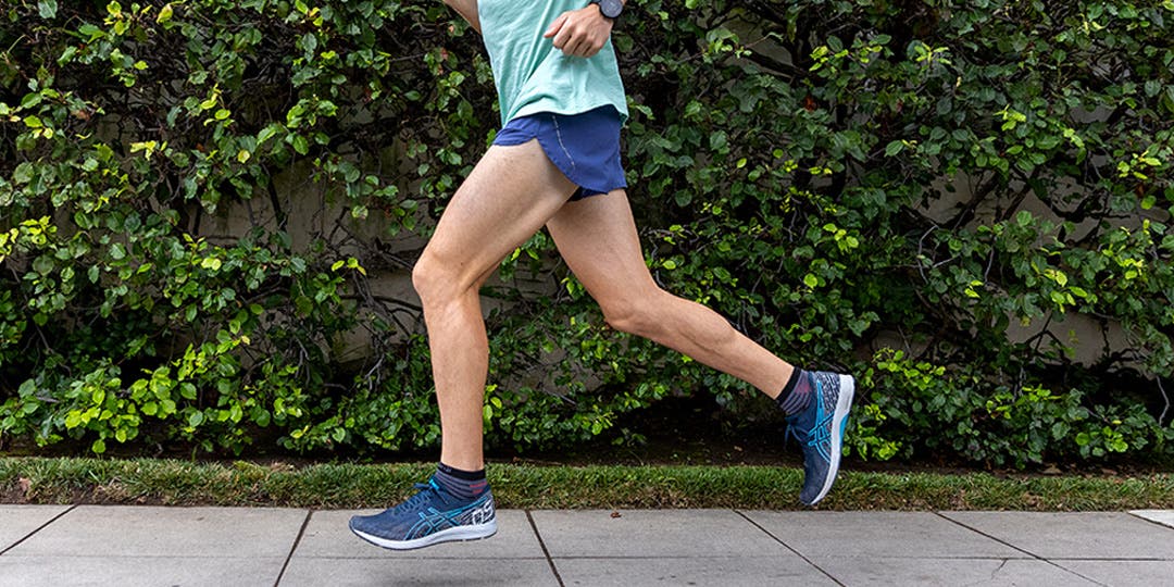 A man wearing running apparel, running shoes, and Injinji peformance socks while running on a sidewalk with a wall of ivy to his side.