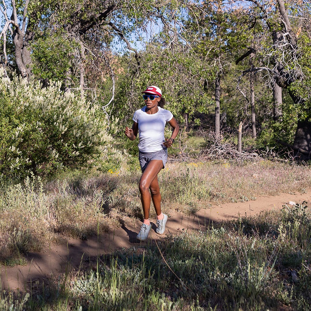 A woman running on a partly shaded trail.