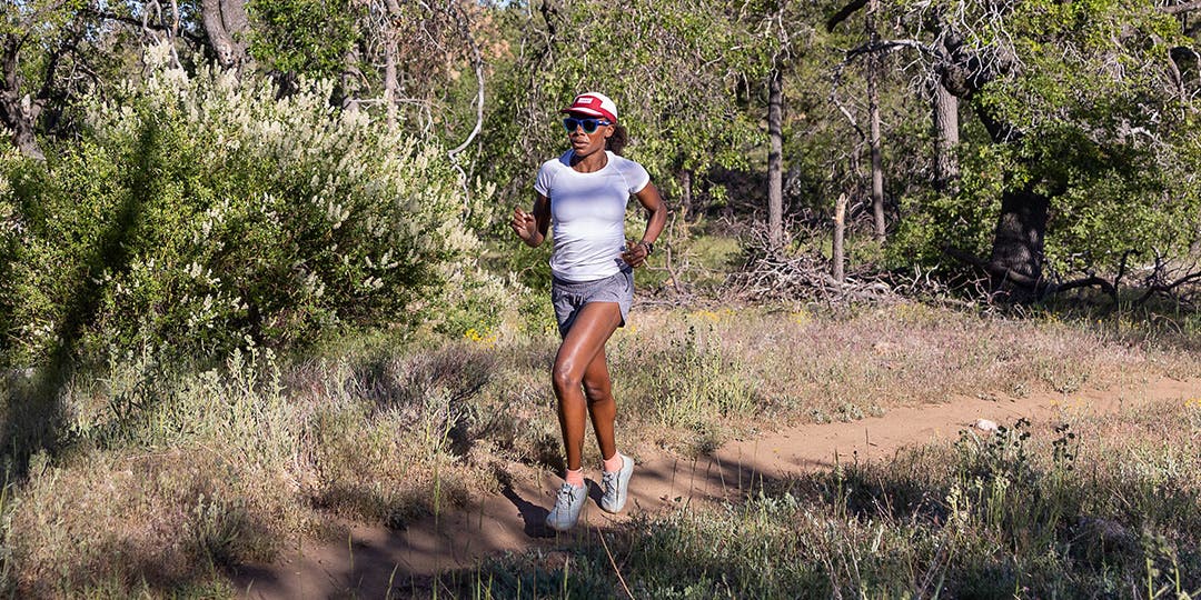 A woman running on a partly shaded trail.