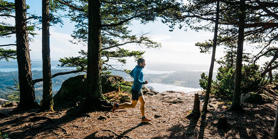 A man running on a forested trail with interconnected lakes in the background. 