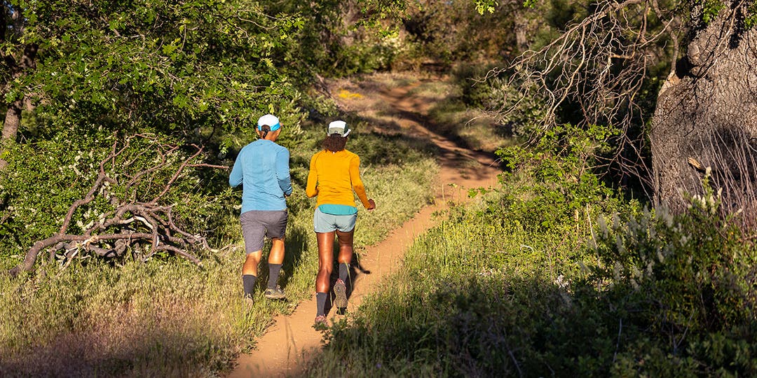 View from behind of two runners side by side on a single track trail. 