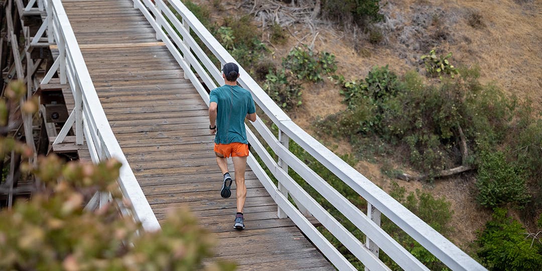 A man running across a wooden bridge in a natural coastal landscape. 