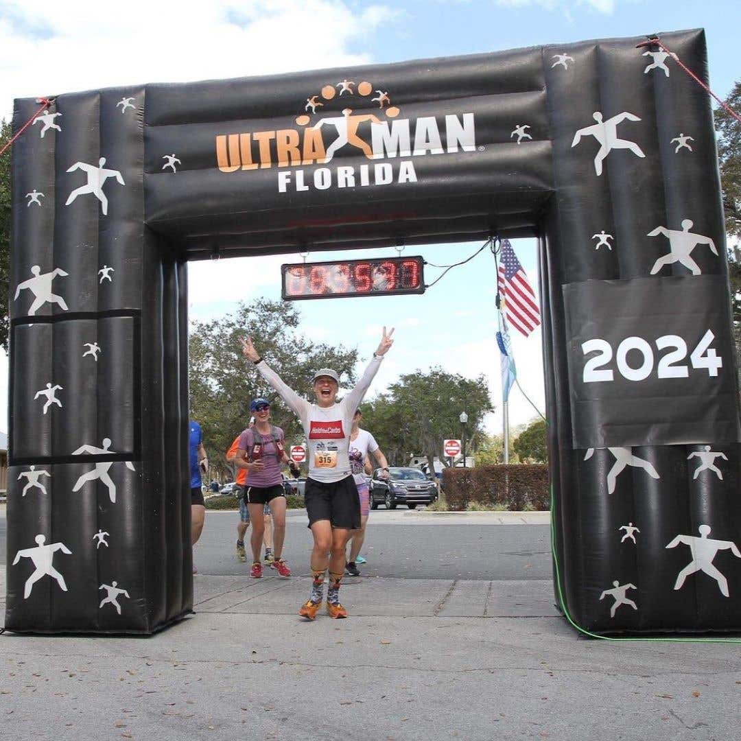 Team Injinji athlete Viktoria Brown holding up her arms in victory at the finish line of the Florida Ultra Man.