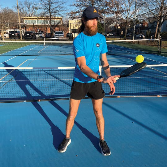 Mike Wardian standing on the edge of an outdoor pickleball court balancing a ball on his paddle.