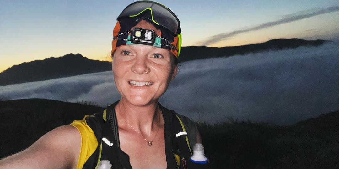 Team Injinji athlete Alyssa Amos on a training run at high altitude wearing a headlamp with the clouds behind her.