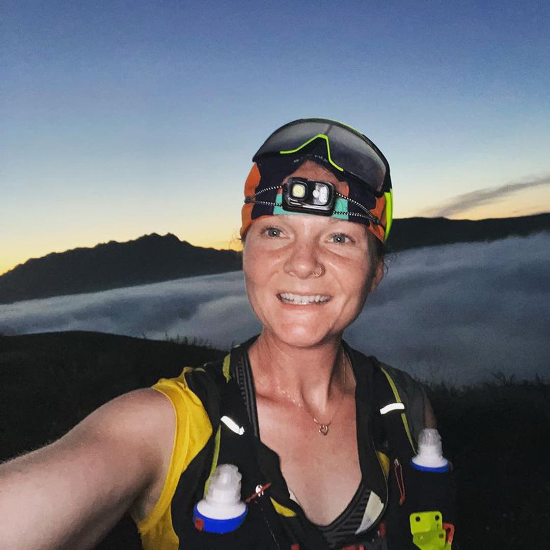 Team Injinji athlete Alyssa Amos on a training run at high altitude wearing a headlamp with the clouds behind her.