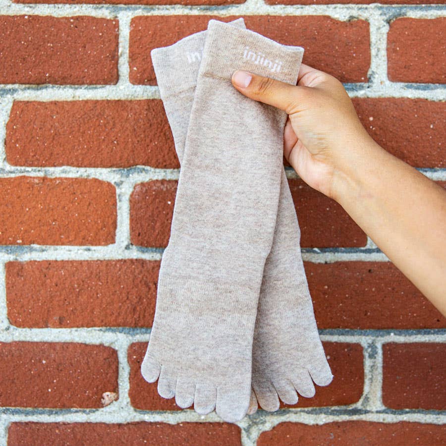 A hand holding a pair of beige everyday toe socks by Injinji