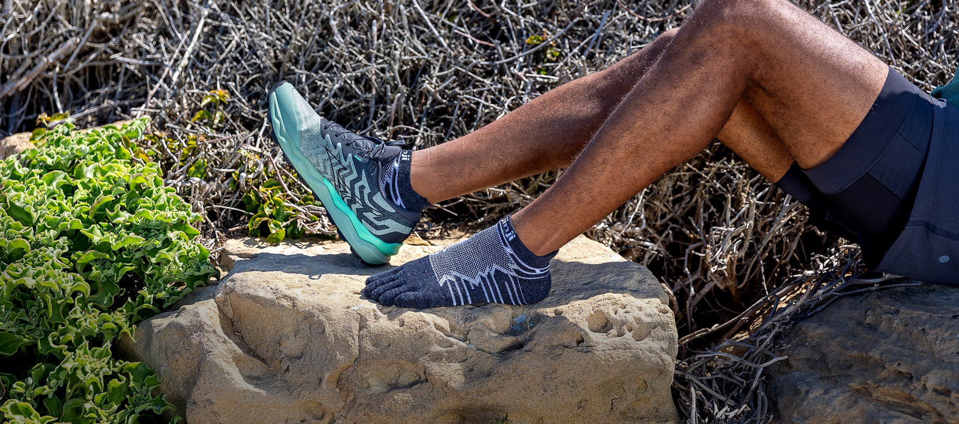 A runner posing on a boulder wearing the new Injinji Ultra Run No-Show Wool toesocks.