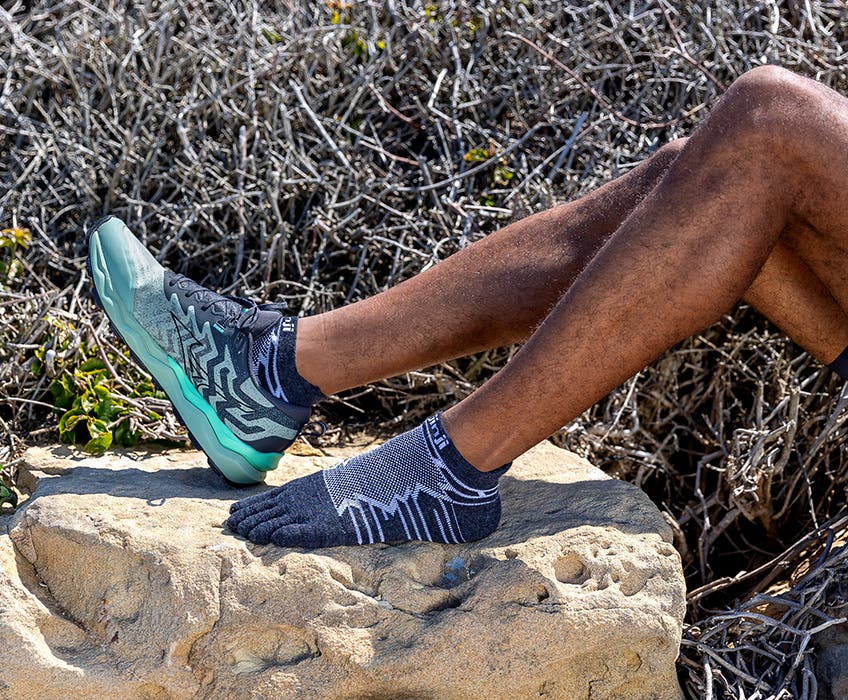 A runner posing on a boulder wearing the new Injinji Ultra Run No-Show Wool toesocks.