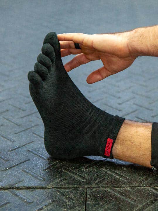 Man stretching his on the floor, touching his toes, wearing the Injinji Sport Original Weight Mini-Crew.