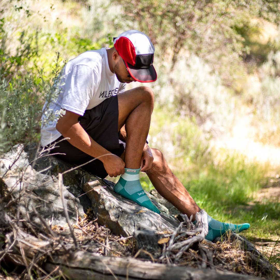 Runner sitting on a rock adjusting his Trail Midweight Mini-Crew toesocks. 