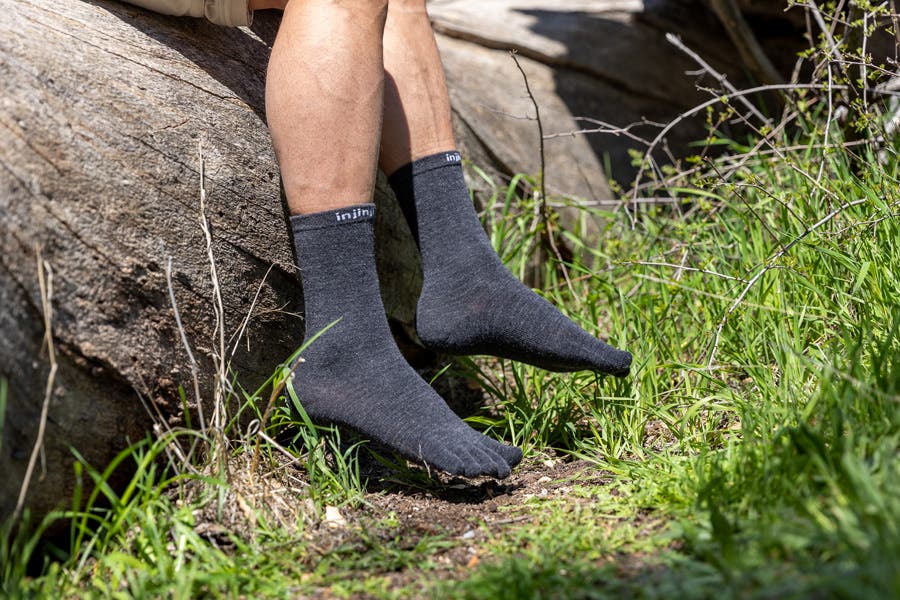 A person sitting on a large rock next to a trail wearing Injinji Liner Crew Wool socks.