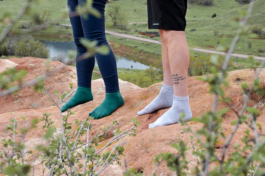 Two people standing on top of a a boulder wearing Injinji Liner Mini-Crew toesocks in Gray and Agave. 