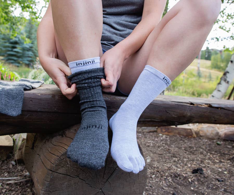 Hiker sitting down, putting on the Hiker crew sock + Liner baselayer sock system. 