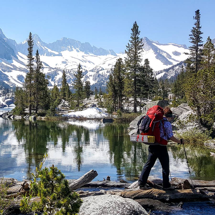 Hiker wearing the Liner + Hiking Crew walking with a lake and trees in the background. 